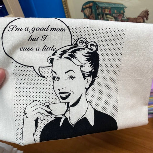 tea towel that shows a women drinking out of a tea cup that says "I'm a good mom, but I cuss a little: slightly flawed kitchen tea towel